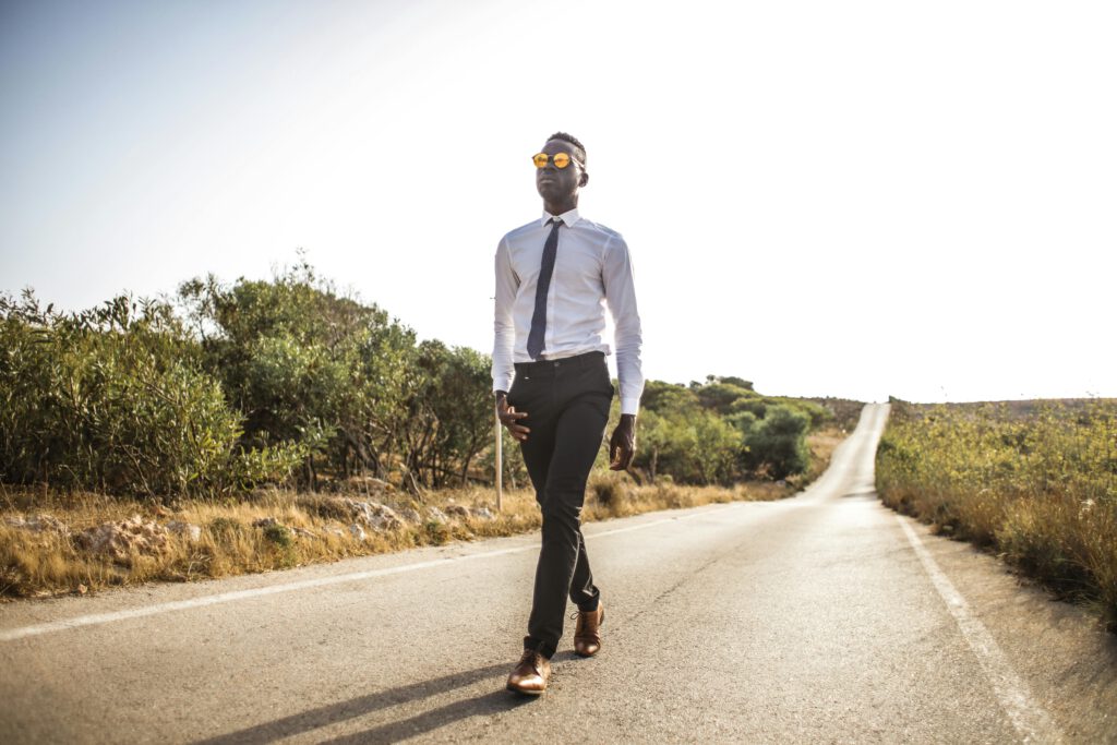 pexels-photo-3760277-3760277 Confident man in a tie walks down an empty scenic road in bright daylight.