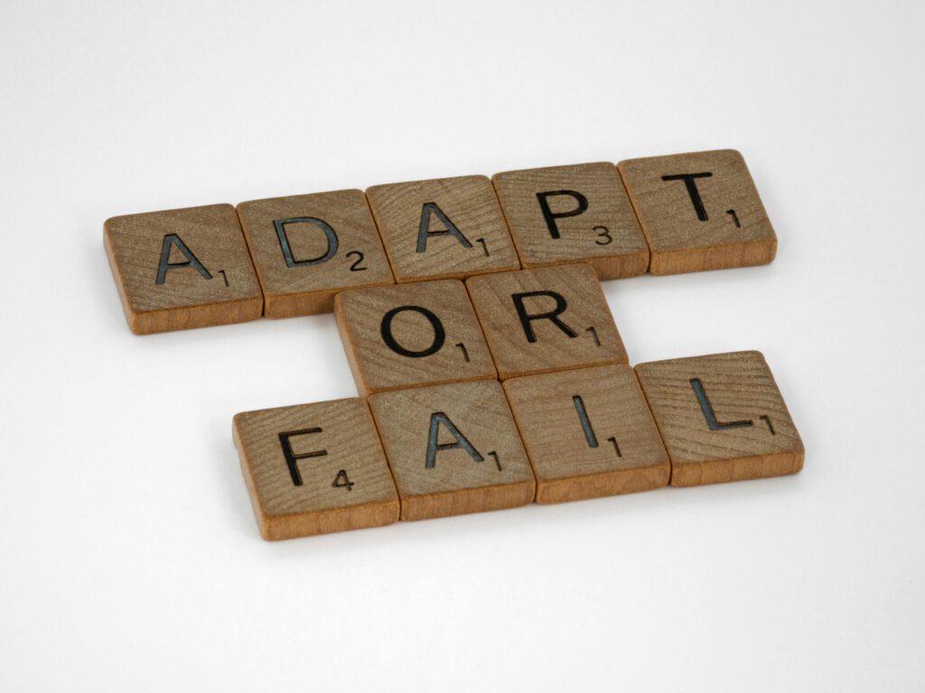 pexels-photo-9141232-9141232 Scrabble tiles spell 'Adapt or Fail' on a white background, conveying a motivational message.